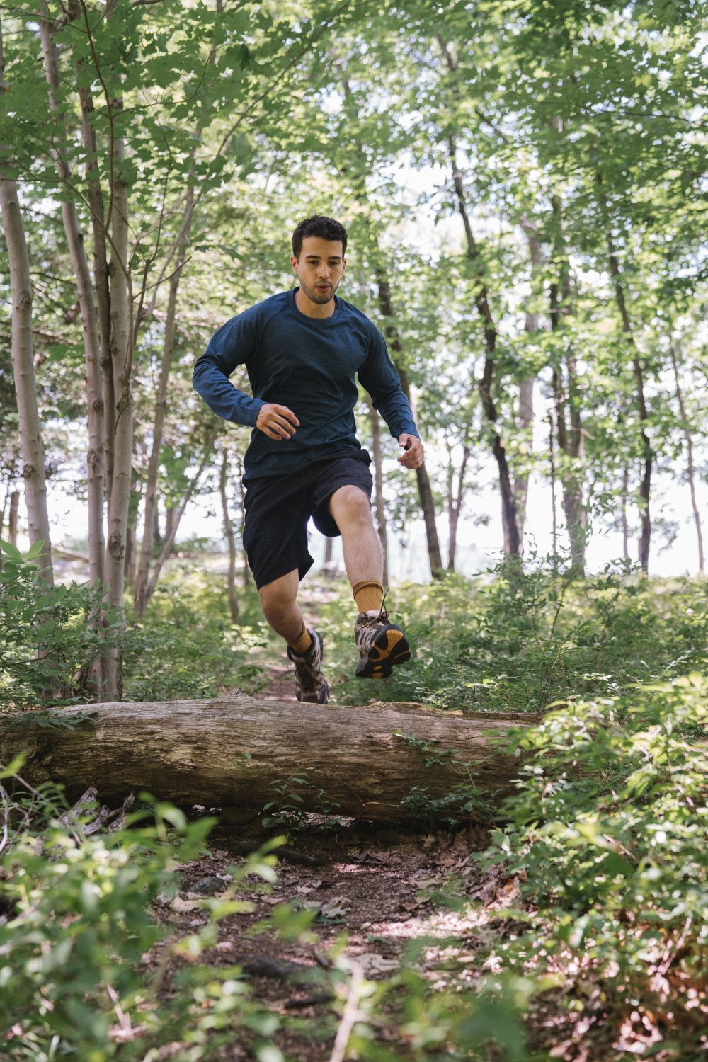 Athletic man jumping over a log during a vibrant forest run in summer