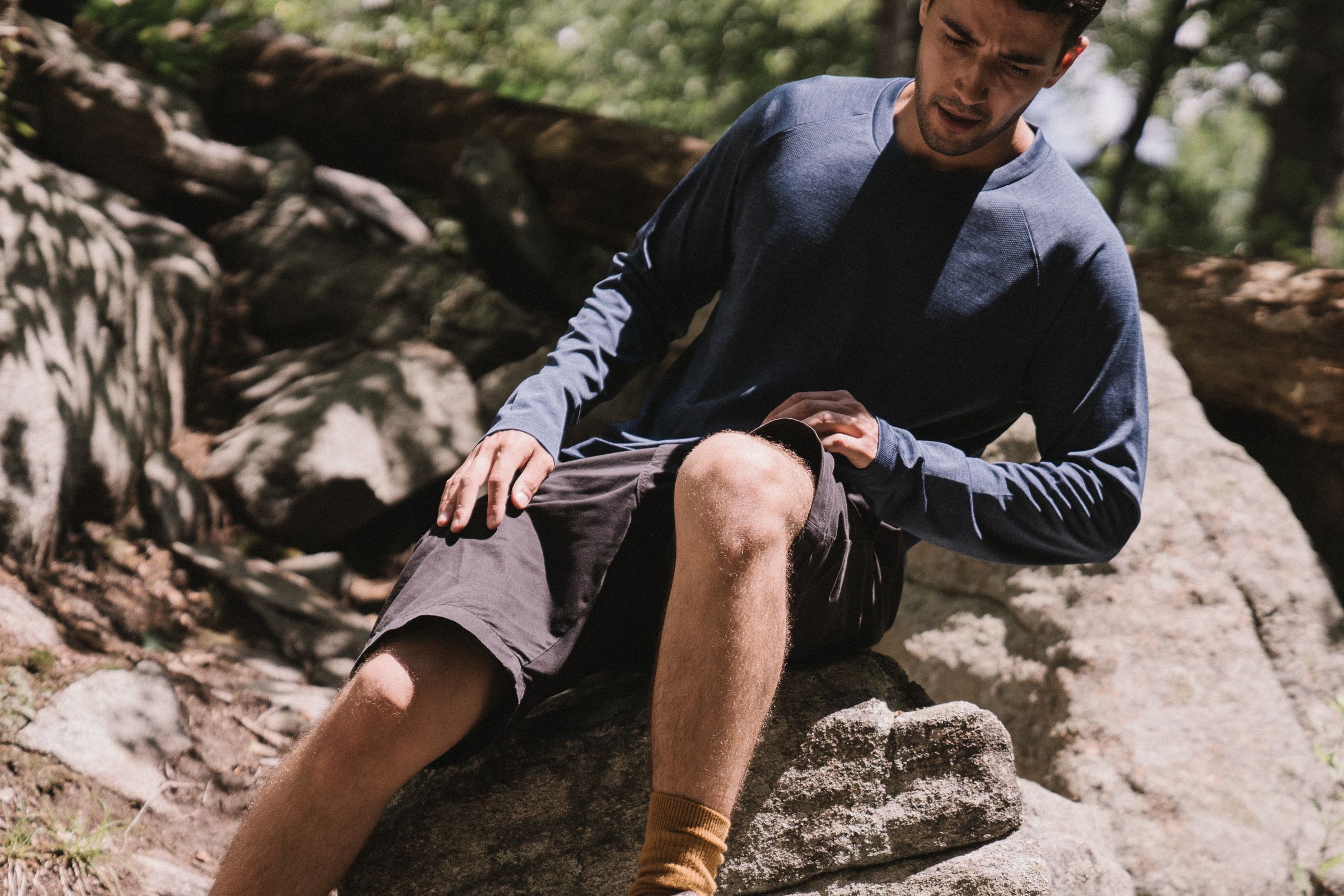 Man in a blue long-sleeve base layer sitting on rocks outdoors