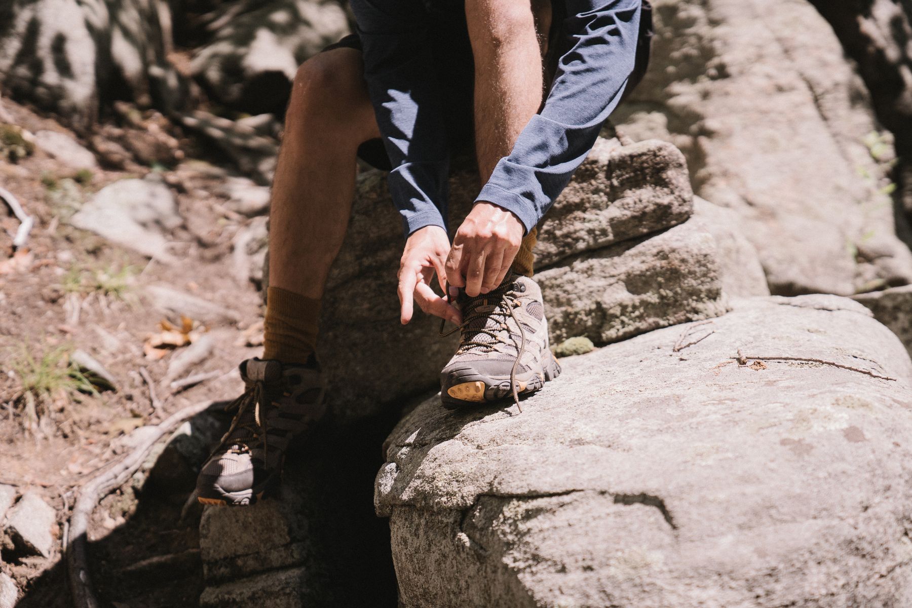 Hiker tying a sneaker on a rocky trail