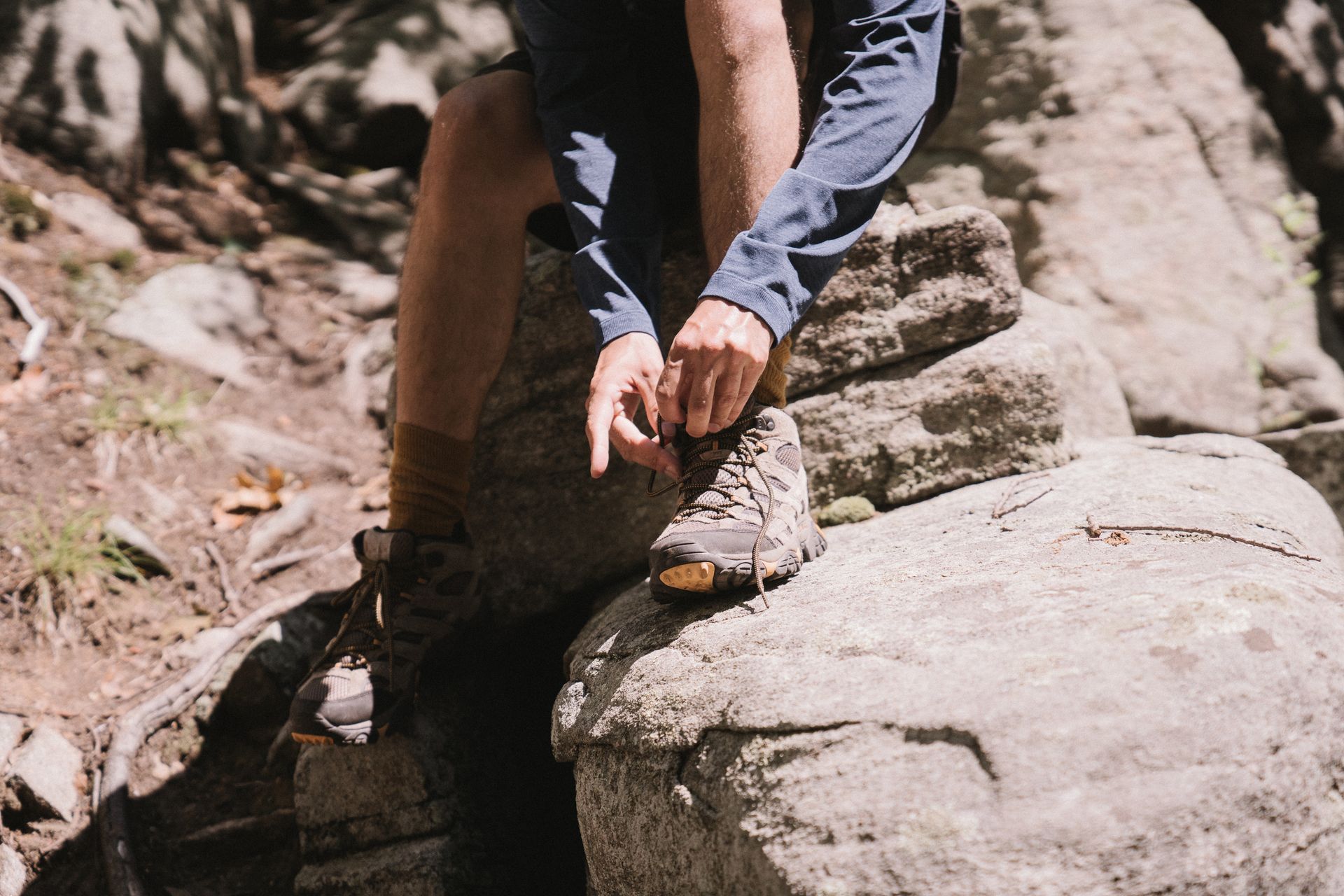 Close-up of a hiker tying boots on a rocky trail, emphasizing outdoor adventure.