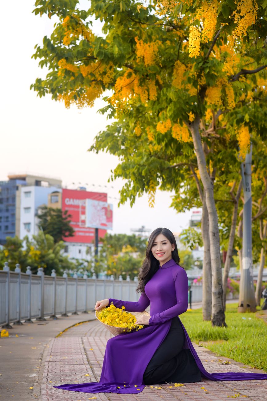 Woman in vibrant purple ao dai poses beneath a blooming tree, embodying elegance and tradition.