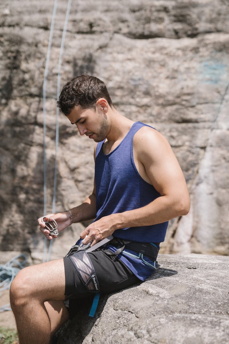 Man In Blue Tank Top And Black Shorts Fixing Climbing Gears 