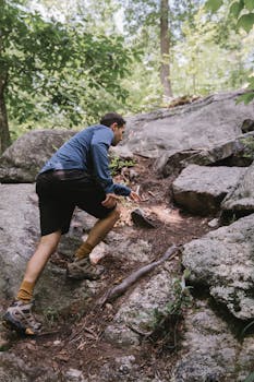 An adventurous man climbing rocky terrain in a lush forest during daytime.