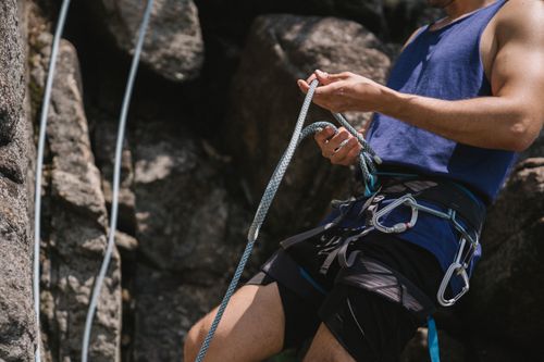Free Man in blue shirt rock climbing, focusing on securing rope against rocky backdrop. Stock Photo