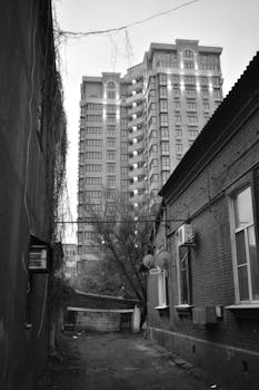 A black and white photo capturing a narrow alley with historic and modern buildings in Krasnodar, Russia.