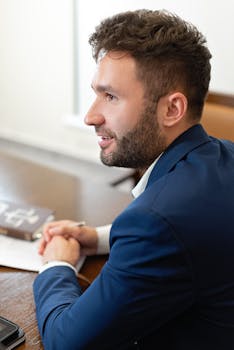 A focused businessman in a blue suit at work, sitting in an office meeting.