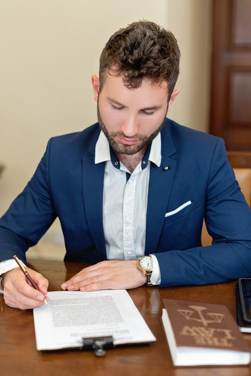 Free A businessman in formal attire signs a legal document at an office desk, emphasizing professionalism. Stock Photo