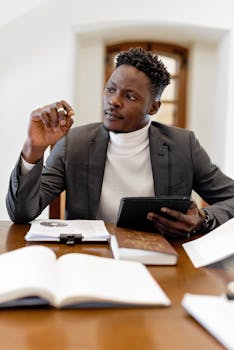 Confident black male professional in office setting consulting a tablet.