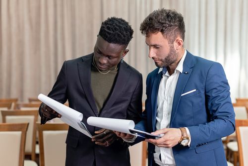 Free Two businessmen in suits reviewing contracts and business documents indoors. Stock Photo