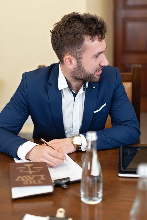 Free Man in blue suit writing at desk with legal book and tablet. Stock Photo