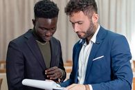 Two businessmen in suits review a contract indoors, focusing on the document.