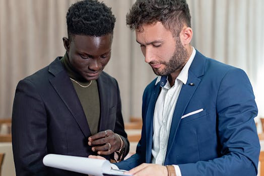 Two businessmen in suits review a contract indoors, focusing on the document.