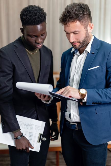 Two business professionals in corporate attire reviewing documents indoors. Two business professionals in corporate attire reviewing documents indoors.