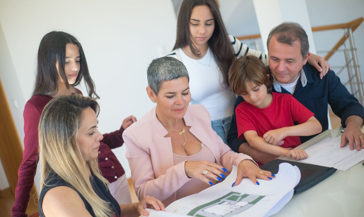 Corretora mostrando planta de imóvel para família em reunião de planejamento patrimonial