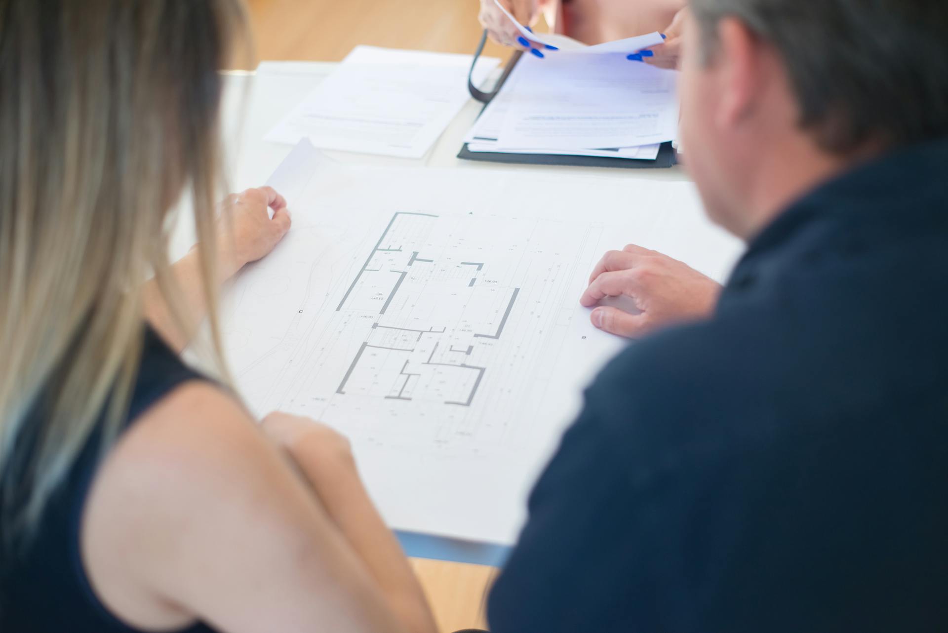 Architects discussing a detailed floor plan in an office setting, viewed from above.