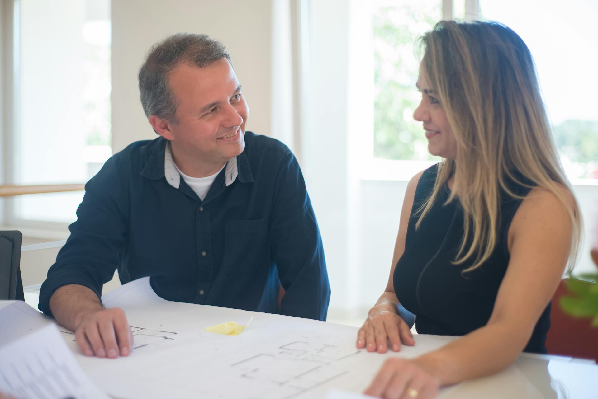 Smiling man and woman reviewing floor plans in a bright office setting.