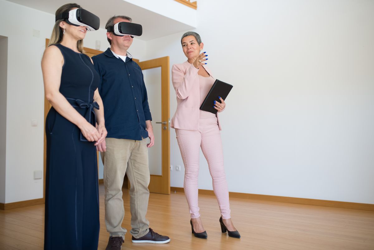 Couple utilisant un casque de réalité virtuelle pour une visite immobilière guidée par un agent