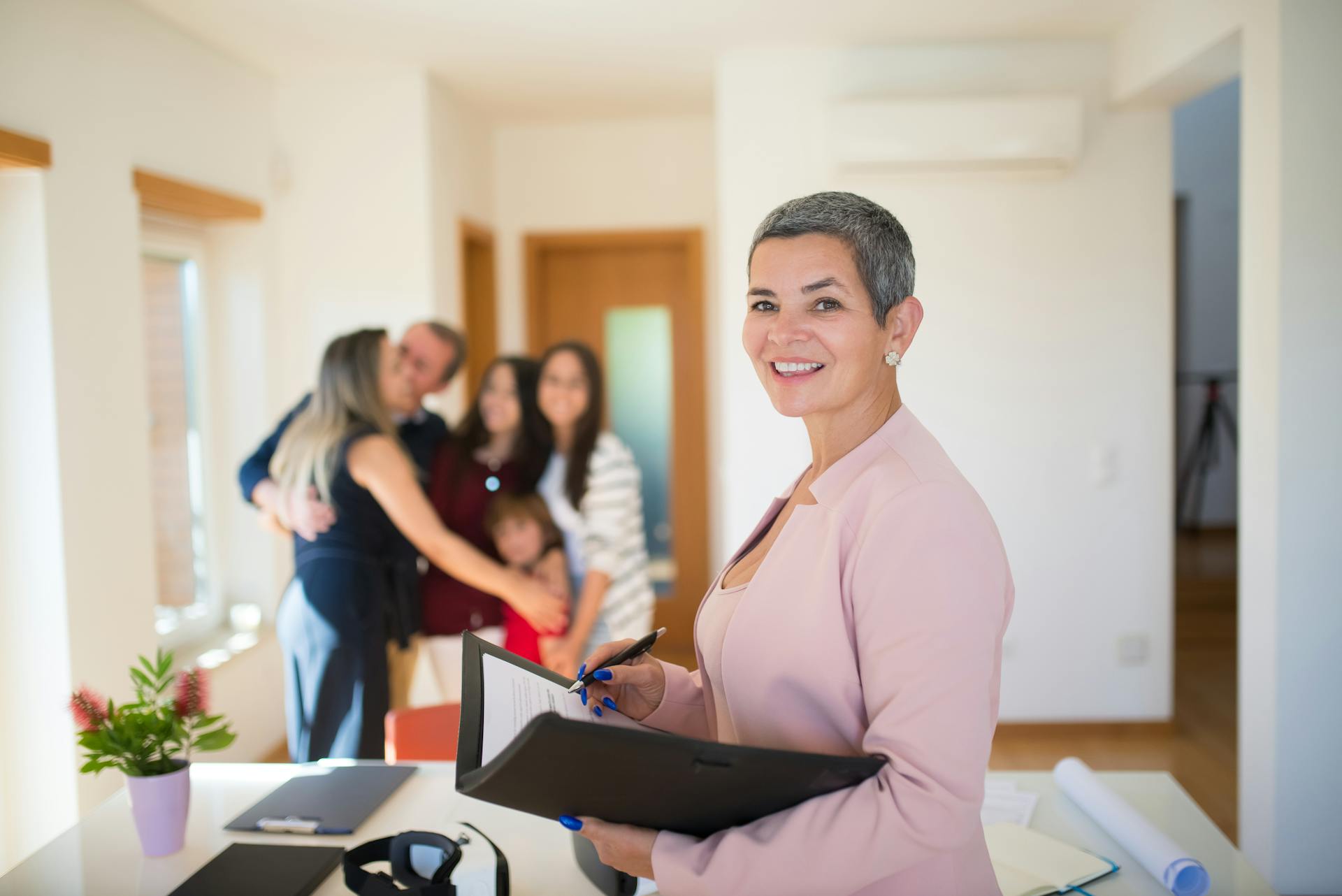 Real Estate Agent Holding Documents and a Family Hugging in the Background