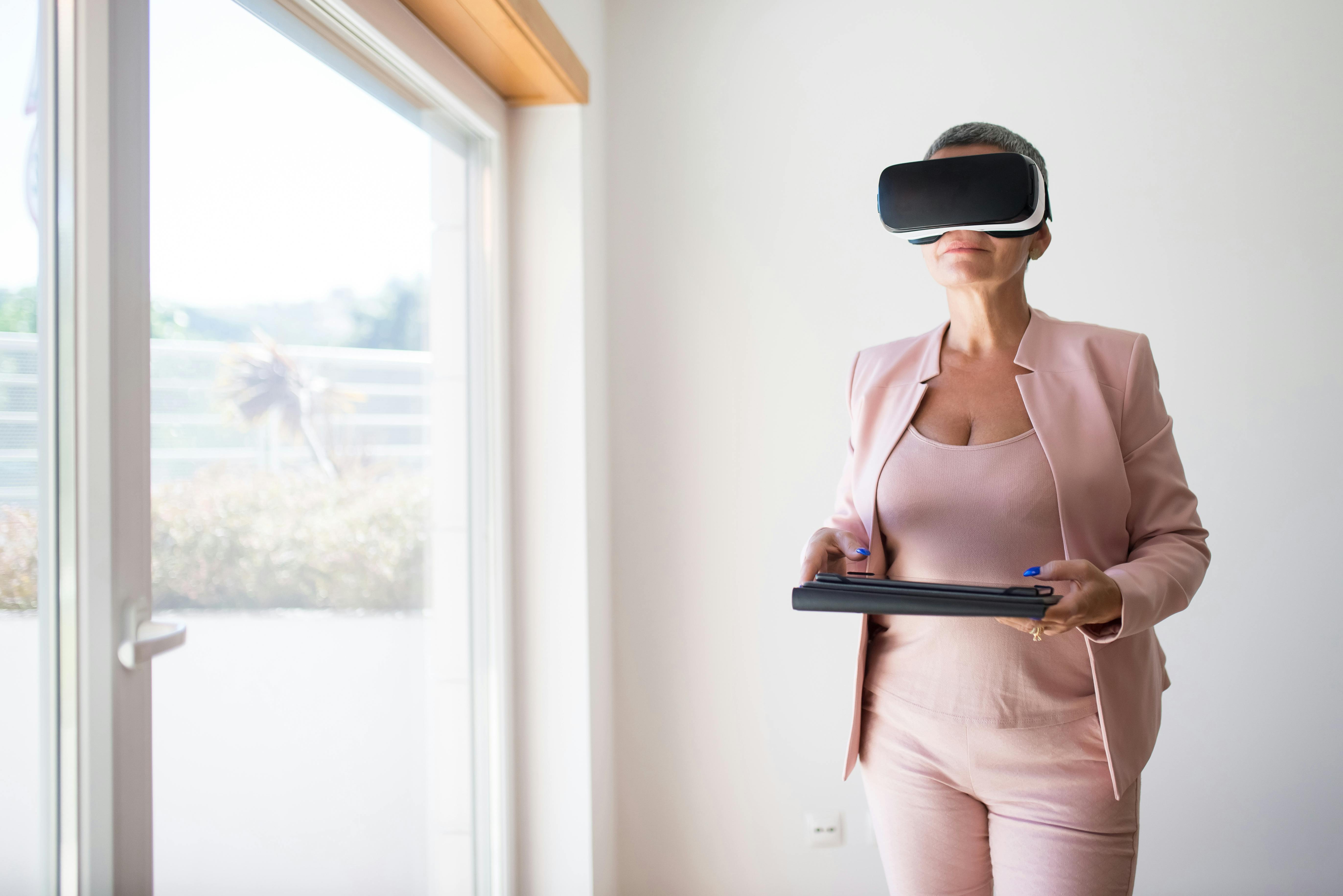 elegant woman wearing vr goggles and holding a tablet while standing in an empty room