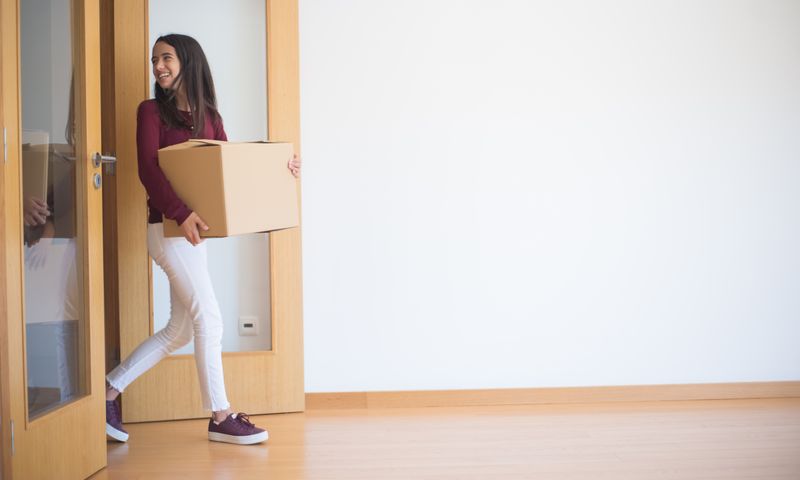 Mulher carregando caixa ao entrar em apartamento novo