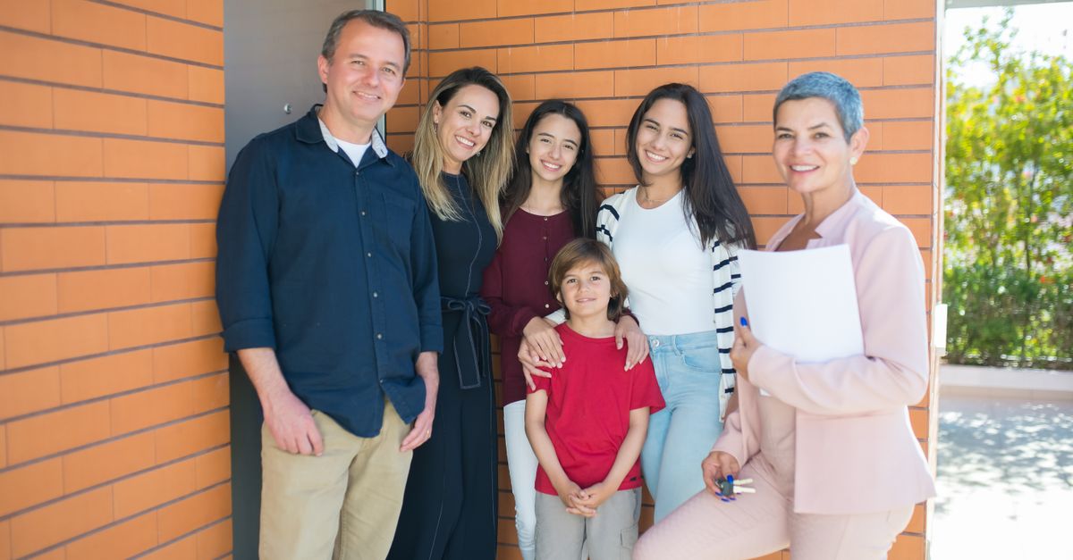 Smiling family with a realtor standing outside their new home, celebrating together.