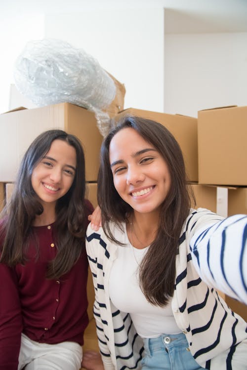 Two Women Smiling and Standing Near Brown Cardboard Boxes