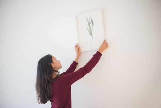 A woman carefully places a minimalist leaf art piece on a white wall.