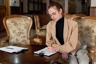 Young woman in a brown blazer signing documents at a table in a stylish office.