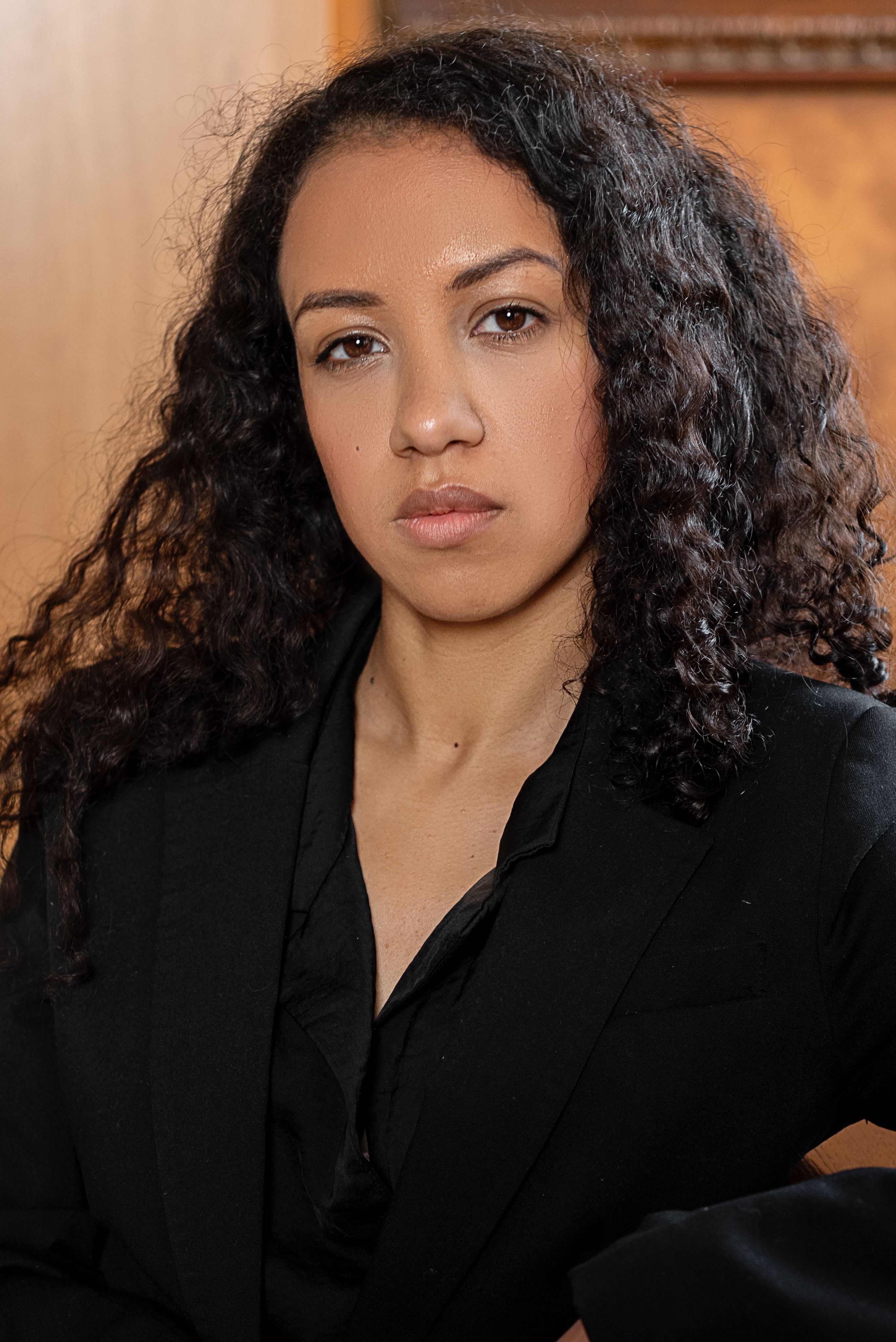 Portrait of a confident woman with curly hair wearing a black blazer, showcasing strength and elegance.