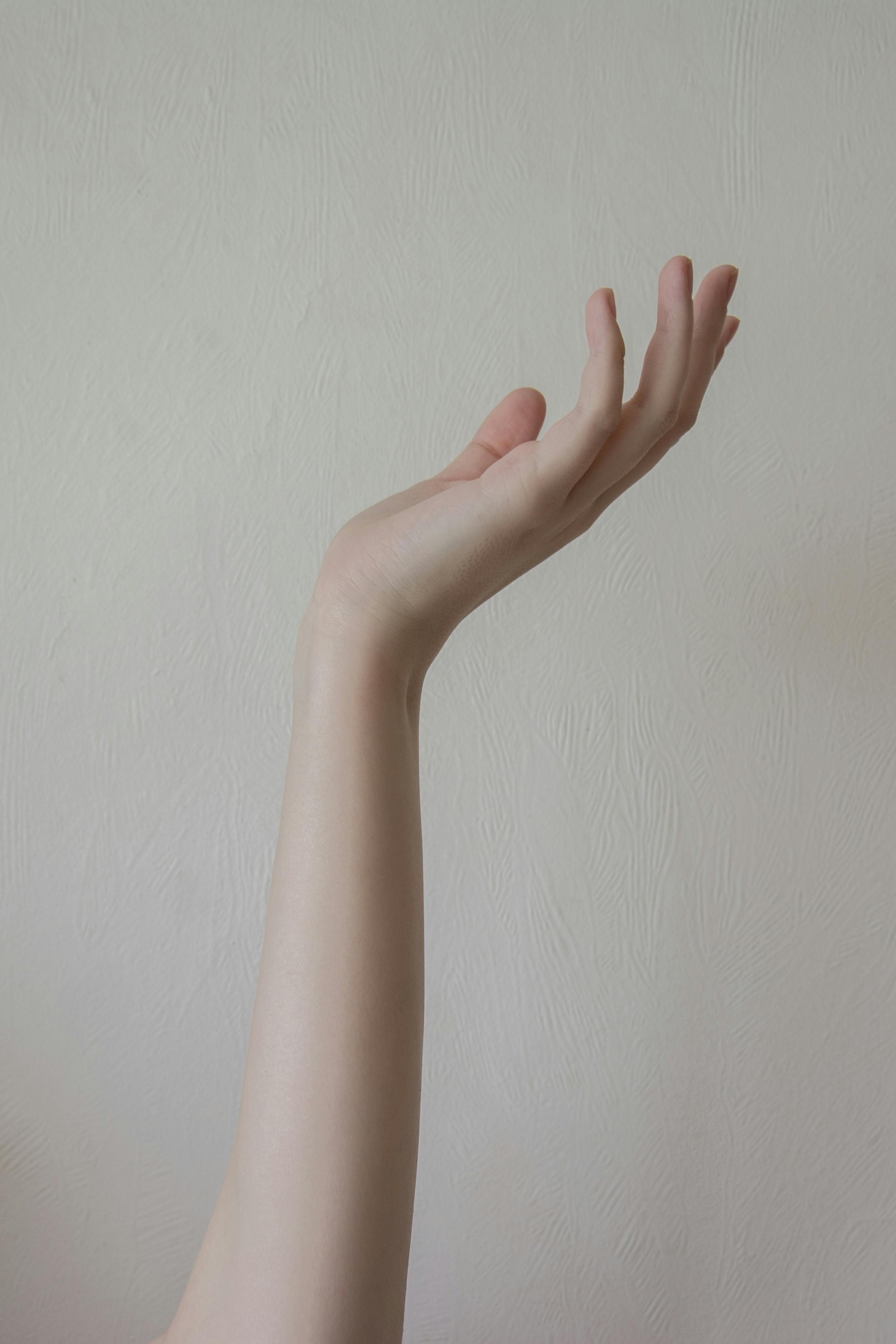 Minimalist photo of a gently posed hand reaching against a neutral background.