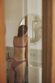 Sensual image of a woman in a bikini looking at herself in a bathroom mirror.