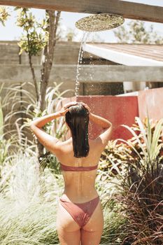 Woman in swimwear enjoying an outdoor shower surrounded by lush greenery.