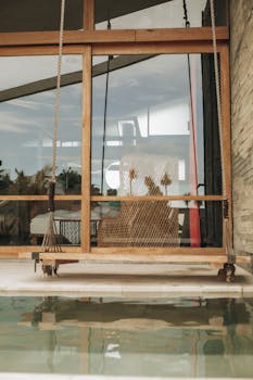 Stylish indoor swing by the pool with a glass reflection, offering a tranquil setting.
