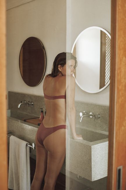 Woman in a swimsuit gazing at her reflection in a bathroom with mirrors.