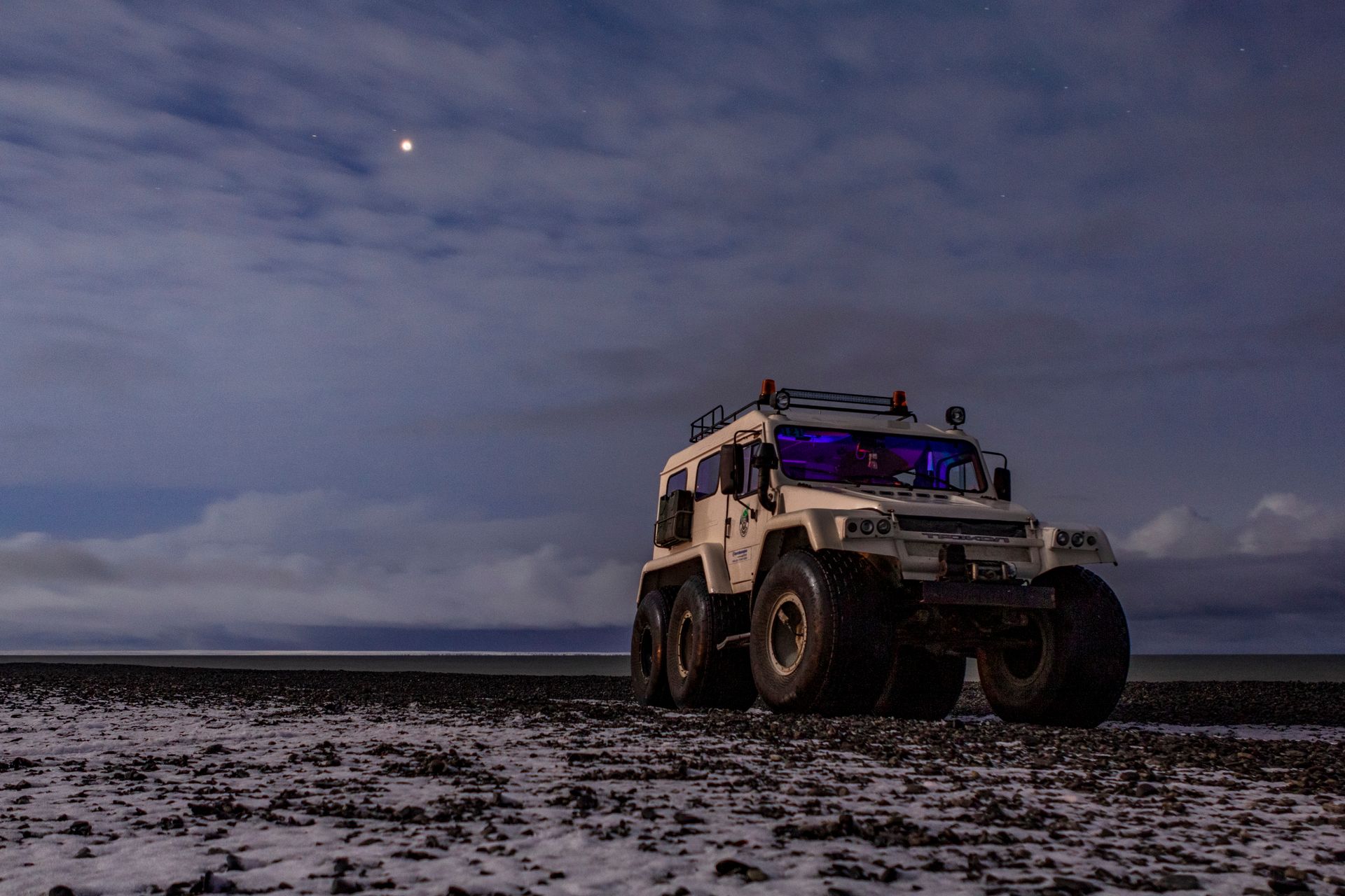A rugged all-terrain vehicle parked on a snow-covered field under a twilight sky.