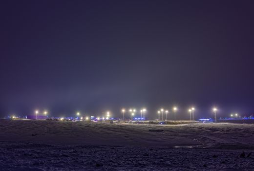 Night view of an illuminated field with industrial lights and distant structures.