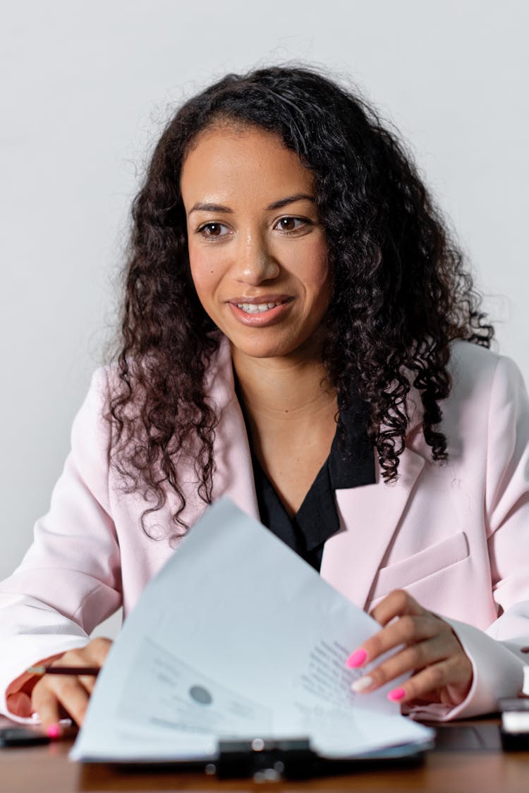 A Woman In A Pink Blazer Reviewing Documents