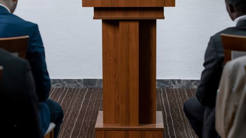 Confident woman speaking at podium addressing an audience in a formal setting.