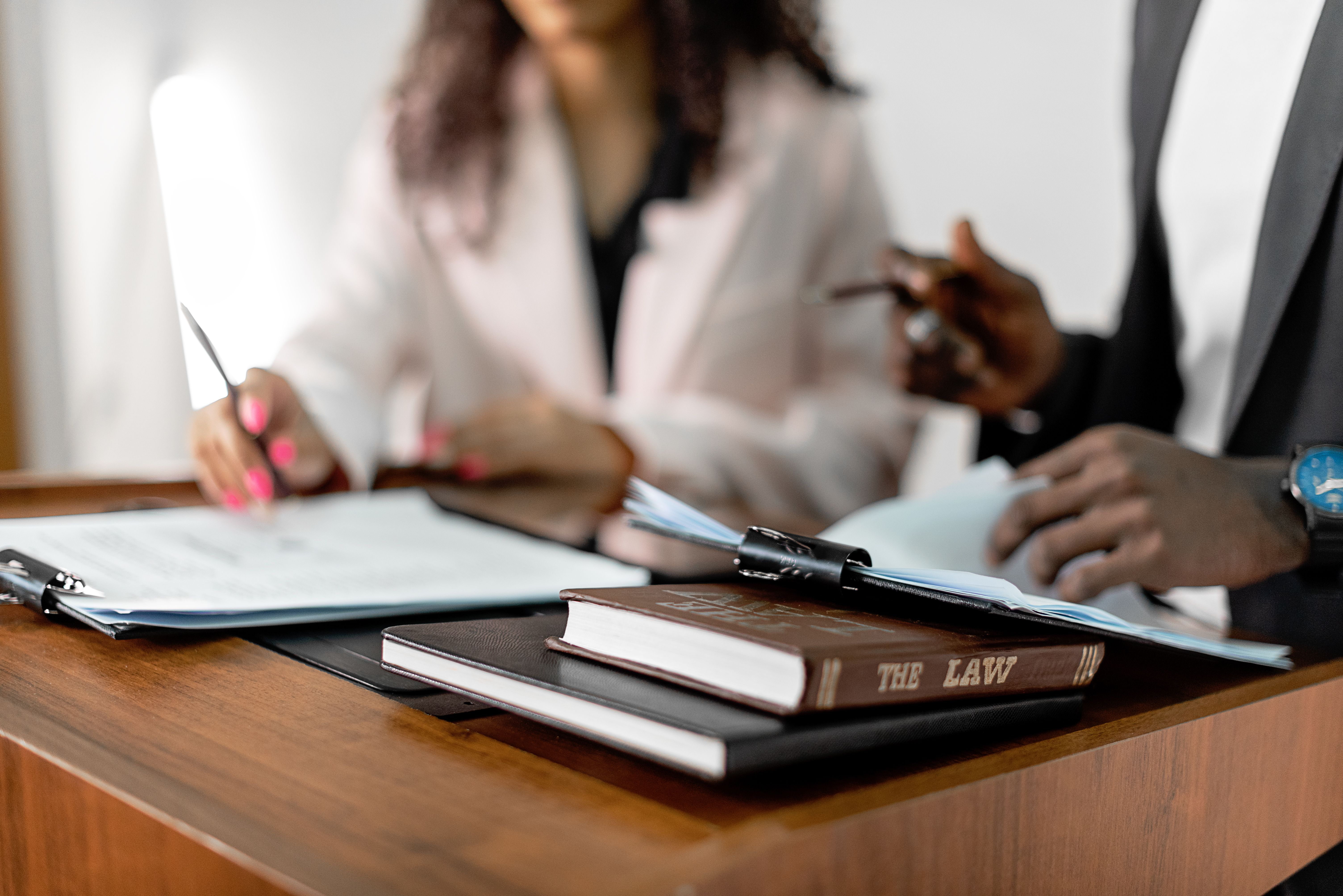 Two legal professionals review documents beside a law book at an office desk