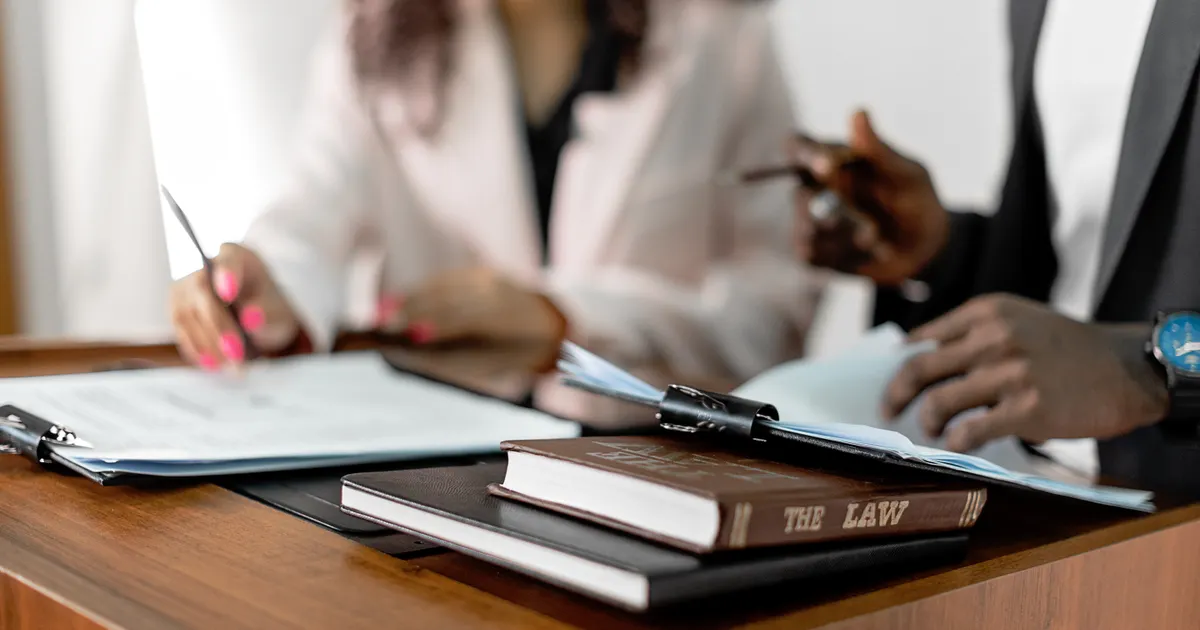 Two women reviewing documents at a desk next to law books, representing a legal review of AI-generated ad creative