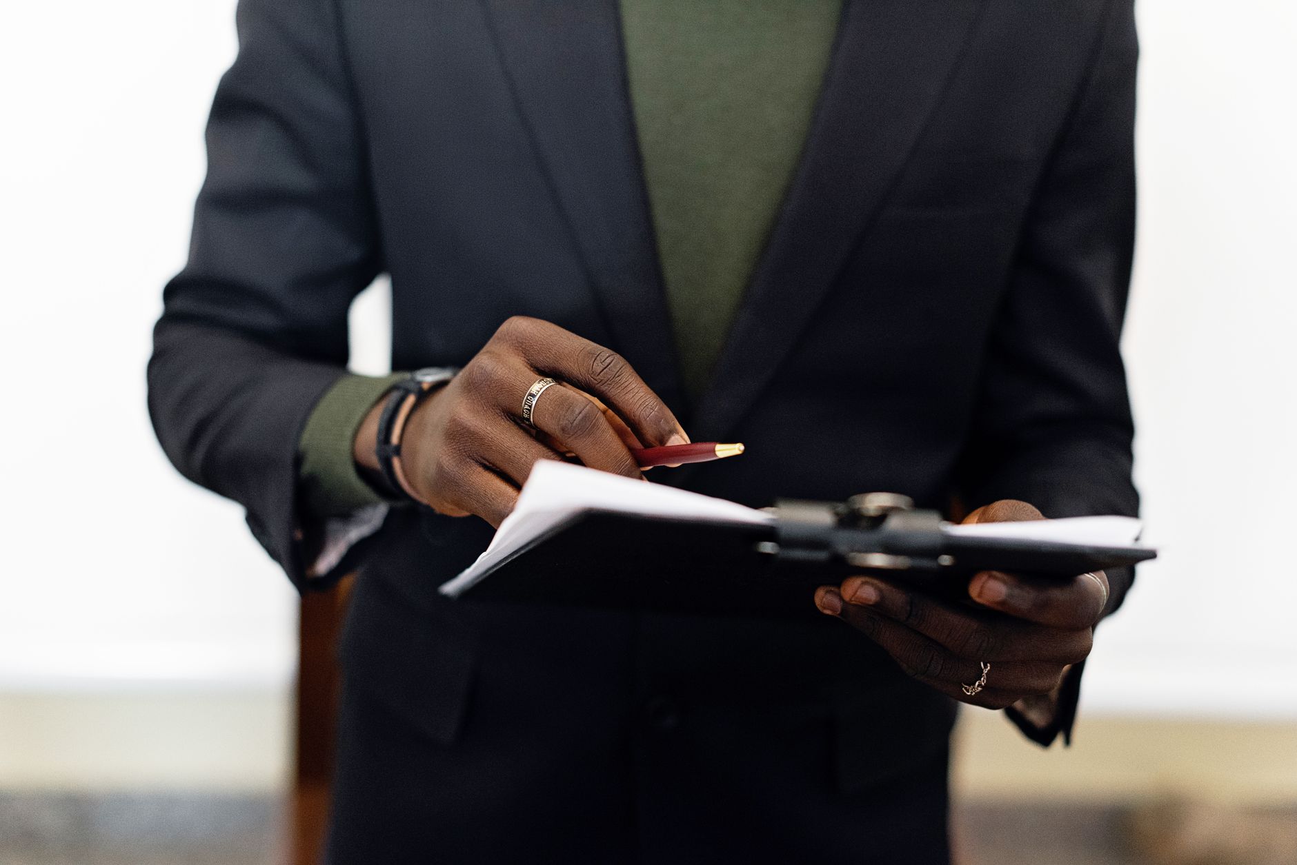Close-up of an adult in a blazer holding a clipboard with documents and a pen indoors.