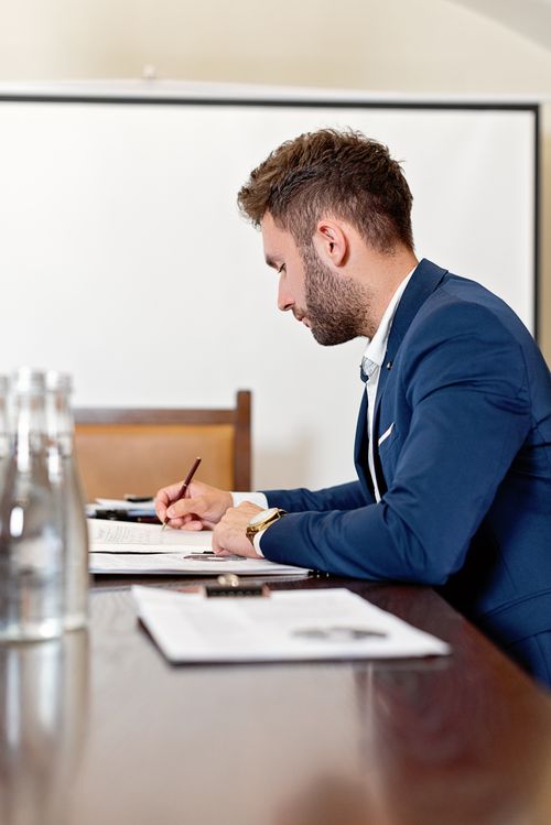 Free A professional man in a blazer takes notes at a conference table. Stock Photo