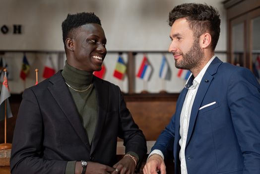 Two smiling businessmen in smart suits engaging in conversation indoors.