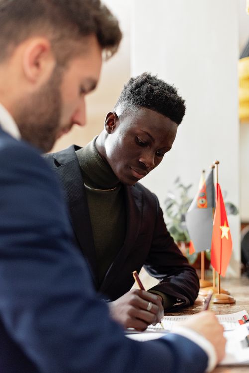 Free Two businessmen in formal wear signing an international agreement with flags on table. Stock Photo