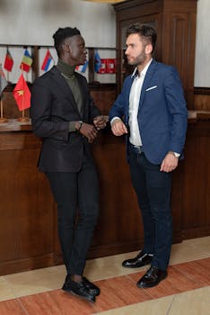 Two businessmen in suits having a conversation indoors, displaying flags in the background.