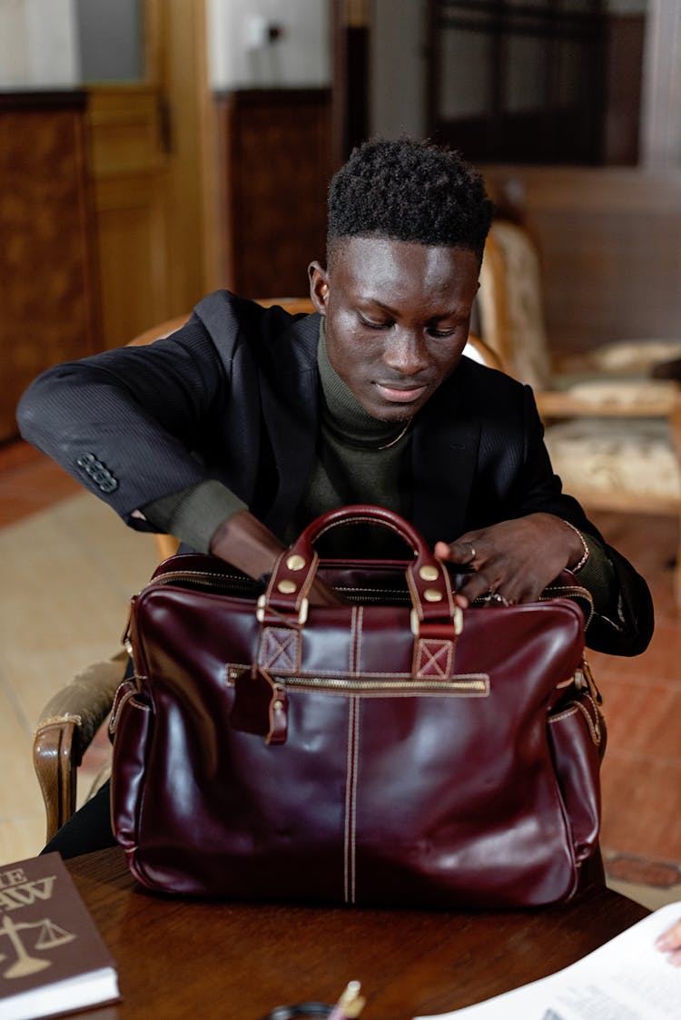 A Man In Black Suit Jacket Looking For Something In A Brown Leather Bag