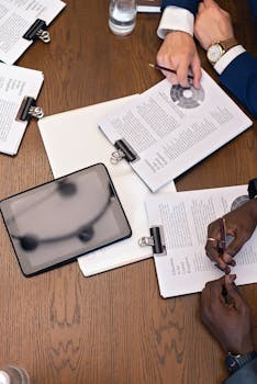 Top view of a business meeting with hands, tablets, and documents on a table.