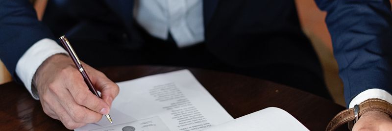A professional individual signs legal documents at a desk in an office setting.