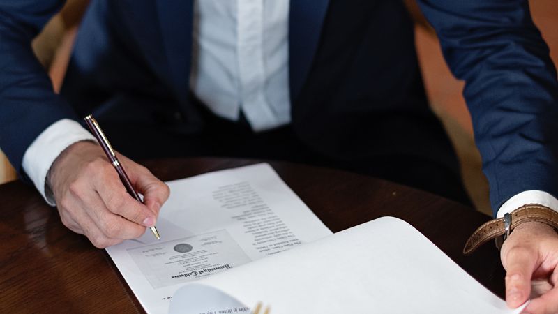 A professional individual signs legal documents at a desk in an office setting.