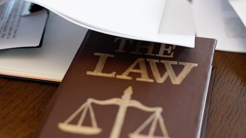 Close-up of a law book with scales icon on a wooden desk covered in papers.